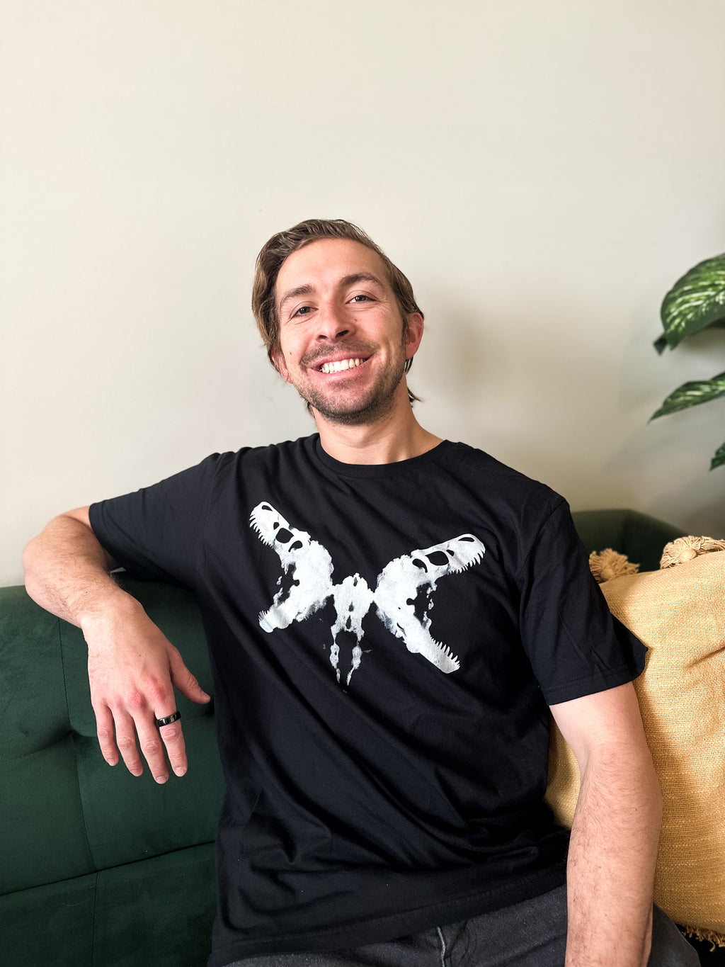A person wearing a black crew neck t-shirt with a white dinosaur skull Rorschach inkblot design.